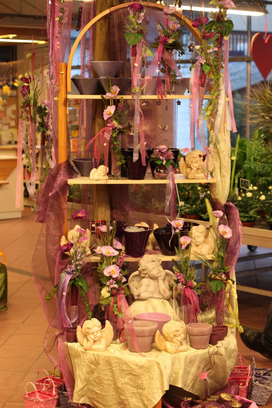 Dekorationsregal mit Engelfiguren, Keramik, Organzabändern und Blumen in Violett- und Rosatönen