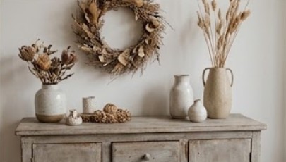 Kranz und Trockenblumen in Keramikvasen auf einer hellen Holzkommode