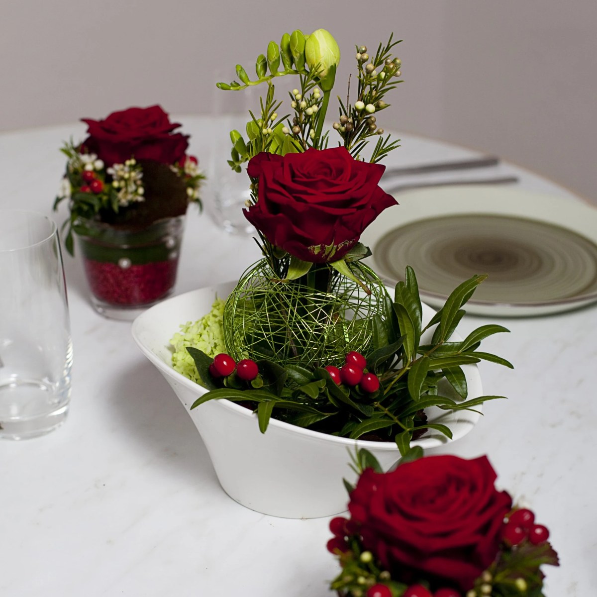 Tischgesteck mit roter Rose, Beeren und grüner Drahtkugel in weißer Schale