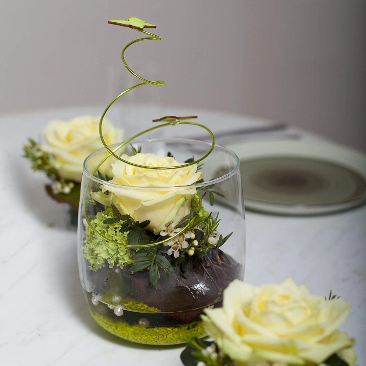 Gelbe Rose im Glas mit Drahtspirale, Schmetterling und Perlen