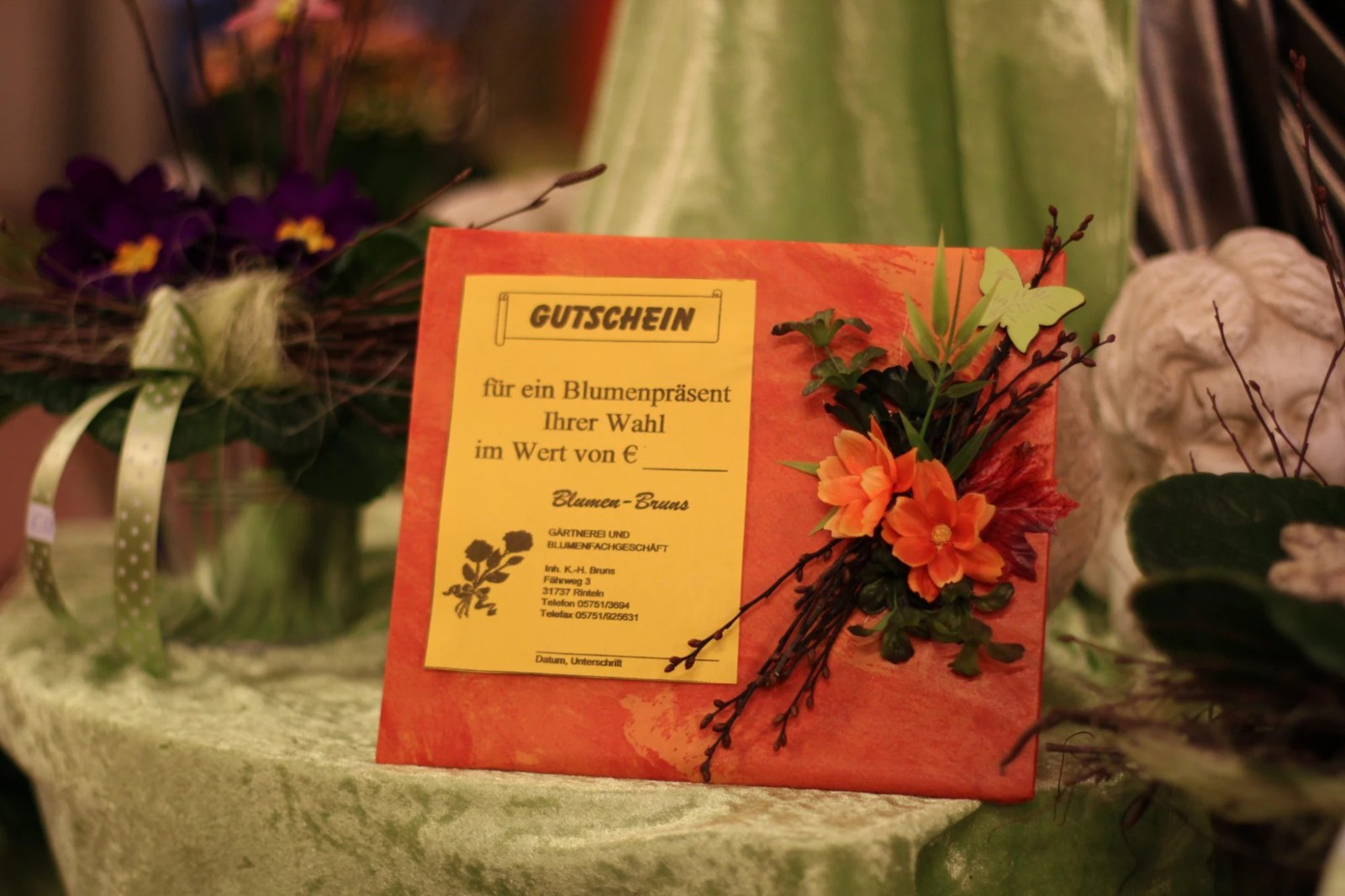 Gutschein in orangem Geschenkumschlag mit orangefarbenen Blüten und Zweigen