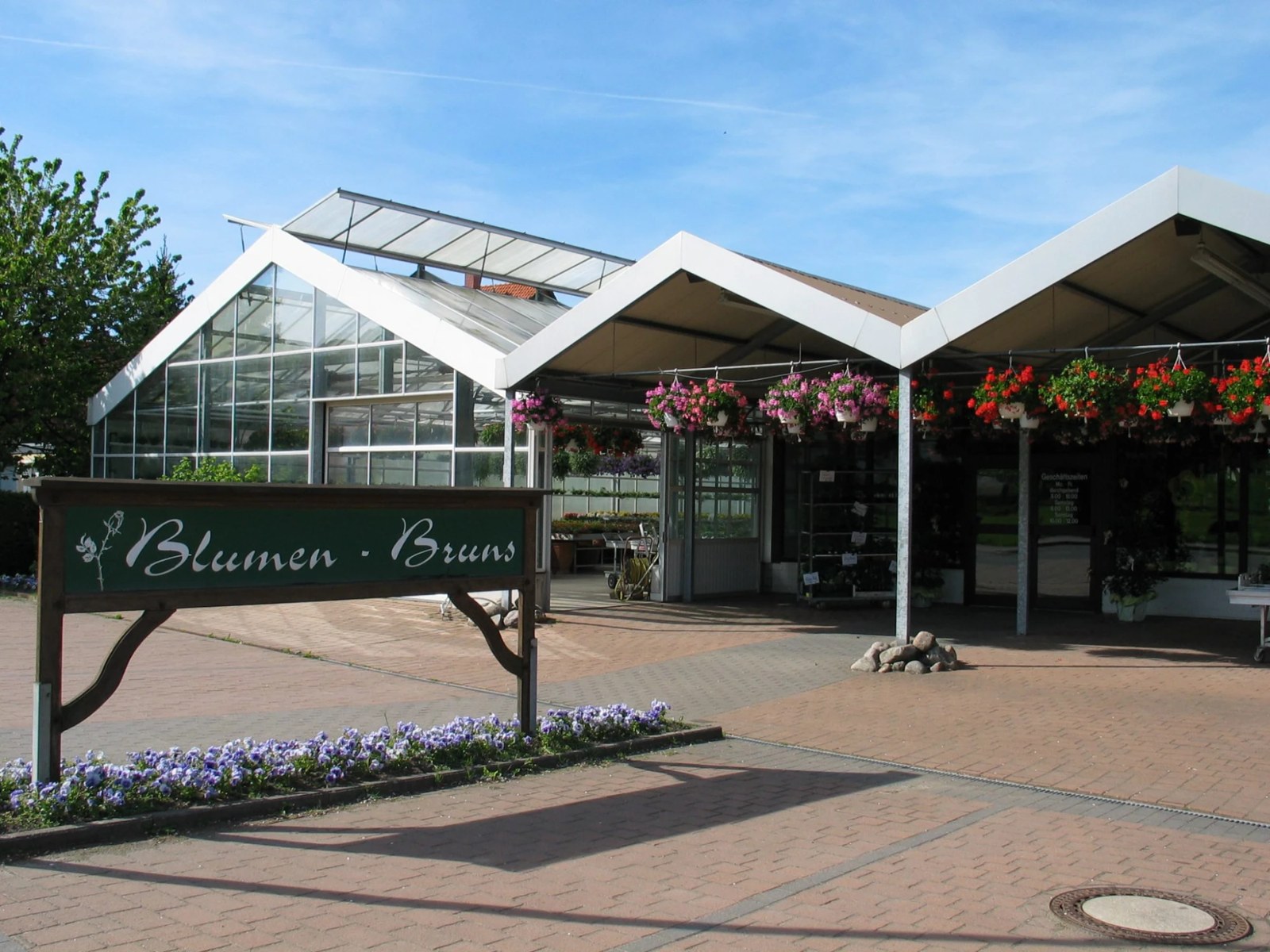 Ladenfront und Gewächshaus von Blumen-Bruns in Hohenrode mit Hängeampeln und Schild