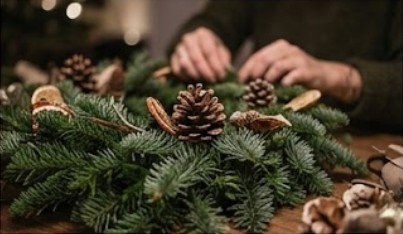 Floristin bindet einen Adventskranz aus Tanne mit Zapfen und getrockneten Orangen